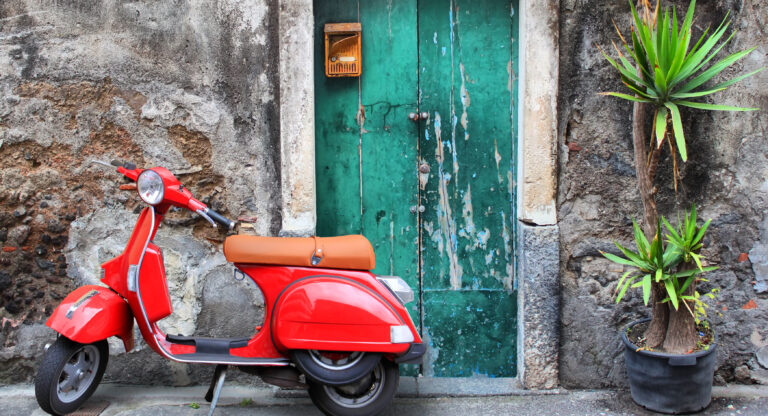 Photo of red scooter near green door and palm