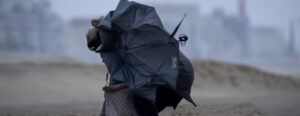 Een foto van een vrouw op het strand met een kapot gewaaide paraplu in de storm, code rood, storm