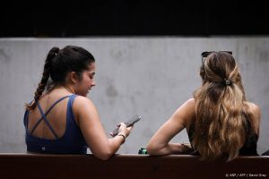 Two women sit on a bench looking at their phone in central Sydney on November 7, 2024.  Australia will move to pass new laws banning children under 16 from social media, Prime Minister Anthony Albanese said, vowing to crack down on tech giants failing to protect vulnerable users.
DAVID GRAY / AFP